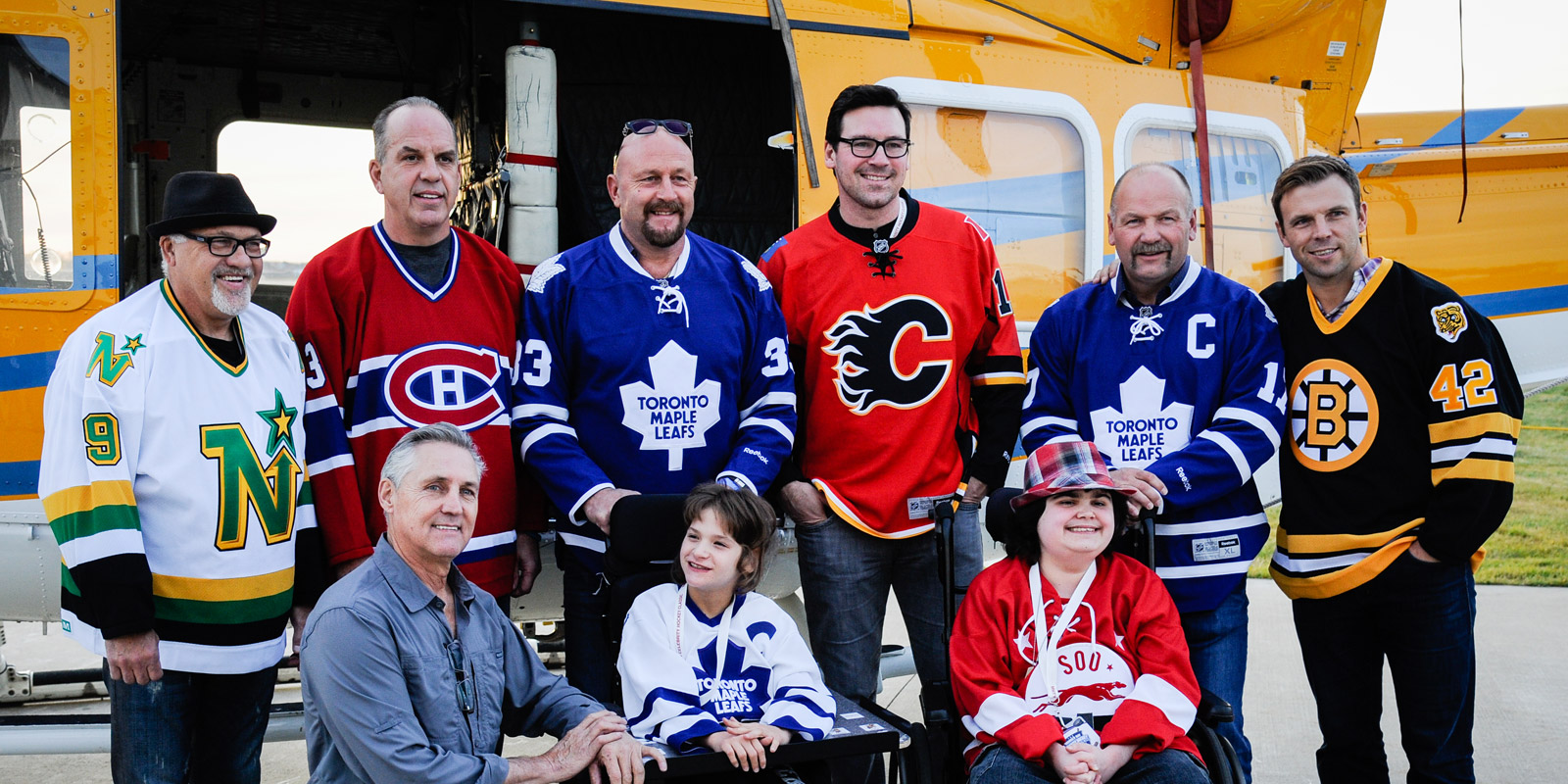 NHL alumni players pose in front of a helicopter with Easter Seals kids